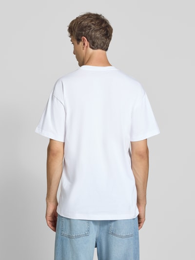 Męski model nosi Regular Fit T-Shirt aus reiner Baumwolle Modell 'Column' von Carhartt Work In Progress, biały, okrągły dekolt, nadruk z napisem i logo, długość tyłu w rozmiarze M: 75 cm, widok całej sylwetki z tyłu.