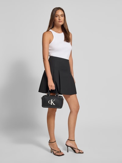 Frauenmodel trägt Crossbody Bag in Leder-Optik von CK Calvin Klein, schwarz mit Logo-Print, Kombi aus Hauptfach und abnehmbarem Schulterriemen, Ganzkörperansicht von vorne.