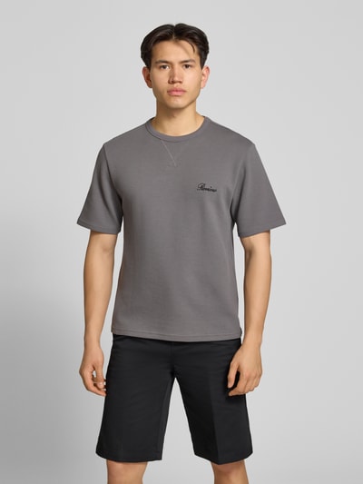 Männermodel trägt T-Shirt mit Label-Stitching von REVIEW, grauer Baumwoll-Mix, Waffelstruktur, gerader Schnitt, Nahaufnahme Oberkörper.
