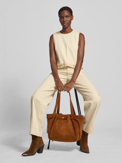 Frauenmodel trägt Tote Bag in Suede-Optik von Tory Burch in warmem Braun mit Magnetverschluss, Logo-Detail und schmalen Schulterriemen, Ganzkörperansicht von vorne.