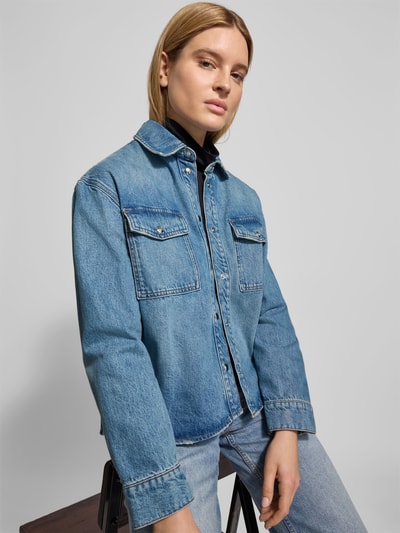Vrouwenmodel draagt Regular Fit Overhemdblouse in Denimlook van Anine Bing, puur katoen, borstzakken, knoopsluiting, Ganzkörperansicht von vorne. Ruglengte maat S: 67 cm, borstwijdte: 62 cm, mouwlengte: 59 cm.