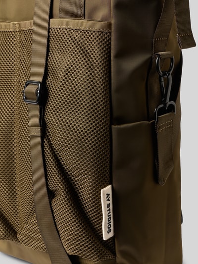 Produktfoto, Rucksack mit Logo-Detail von AY STUDIOS in Olivgrün mit Netz-Taschen, Reißverschluss und verstellbaren Schulterriemen, Detailaufnahme.