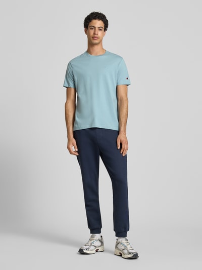 Mannenmodel draagt T-shirt met Label-Stitchings en ronde hals van CHAMPION in lichtblauw, puur katoen, regular fit, ruglengte maat M 66 cm. Volledige lichaamsaanzicht van voren.
