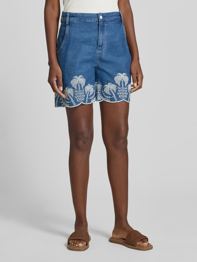 Frauenmodel trägt Shorts mit Lochstickerei Modell 'PILAR' von Guess aus reiner Baumwolle im Wide-Fit, blaue Textur, französische Eingrifftaschen, Gesäßtaschen, Knopf- und Reißverschluss, Ganzkörperansicht von vorne.