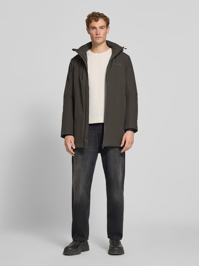 Męski model nosi Regular Fit Parka mit Logo-Print von Lindbergh z elastycznej mieszanki materiałów, czarny, przód, ujęcie całej sylwetki. Długość tyłu w rozmiarze M: 90 cm, szerokość ramion w rozmiarze M: 50 cm, szerokość klatki piersiowej w rozmiarze M: 58 cm, długość rękawów w rozmiarze M: 65 cm.