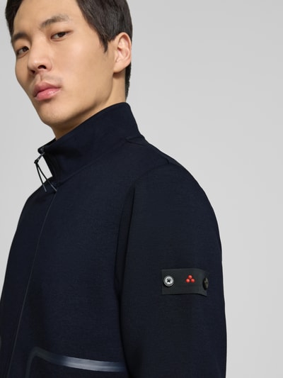 Męski model nosi Regular Fit Jacke mit Stehkragen Modell 'Scott' od Peuterey, granatowy kolor, elastyczny materiał z bawełną, widoczne kieszenie i naszywka na rękawie, krój regular fit, dwukierunkowy zamek, elastyczne wykończenia, długość tyłu i rękawa w rozmiarze M: 66 cm, zbliżenie na górną część ciała, widok z przodu.