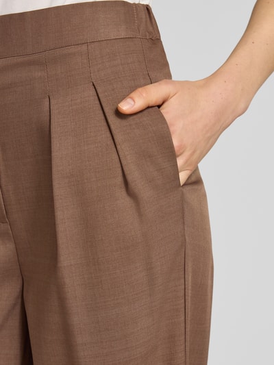 Frauenmodel trägt Stoffhose mit gelegten Falten von Little Mistress in Braun, glatte Textur, Detailaufnahme Nahaufnahme Hüfte