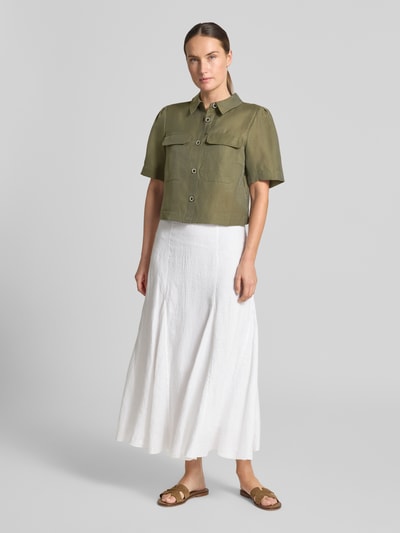Frauenmodel trägt Regular Fit Bluse aus Lyocell-Mix mit Brusttaschen von MORE & MORE in Olivgrün, kombiniert mit weißem Rock, Ganzkörperansicht von vorne. Bluse mit Hemdblusenkragen, Knopfleiste, Brusttaschen, Leinen-Anteil, Rückenlänge 45 cm, Ärmellänge 28 cm.