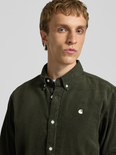 Männermodel trägt Regular Fit Freizeithemd aus Cord mit Button-Down-Kragen von Carhartt Work In Progress in Dunkelgrün, Reine Baumwolle, Label-Stitching, Nahaufnahme Oberkörper.