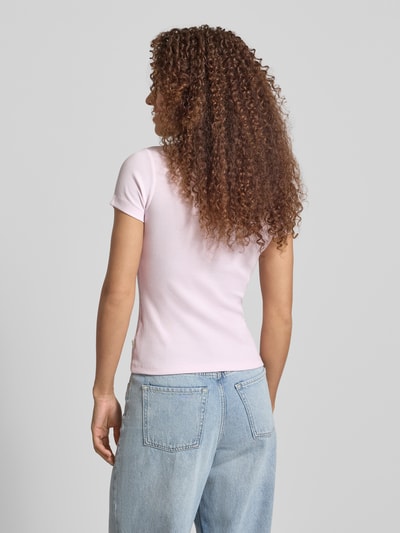 Frauenmodel trägt T-Shirt in Ripp-Optik mit Logo von Guess Jeans in zartem Rosa, Baumwoll-Elasthan-Mix, Rückansicht Ganzkörperansicht.