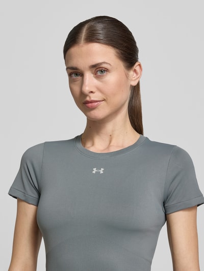 Vrouwenmodel draagt T-shirt met ronde hals en logo van Under Armour, materiaalmix met stretch, slim fit, ruglengte maat S 54 cm, close-up bovenlichaam.