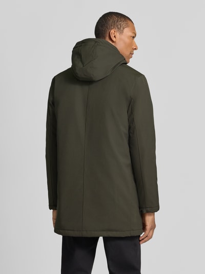Męski model nosi Jacke mit Eingrifftaschen Modell 'Madeston' od Matinique, kolor ciemnozielony, materiał z domieszką stretchu, krój regular fit, kaptur z tunelem, ukryty zamek, kieszenie boczne, detal z logo, długość tyłu 86 cm, szerokość ramion w rozmiarze M: 46 cm, szerokość klatki piersiowej w rozmiarze M: 53 cm, długość rękawa w rozmiarze M: 66 cm, pełny widok od tyłu.