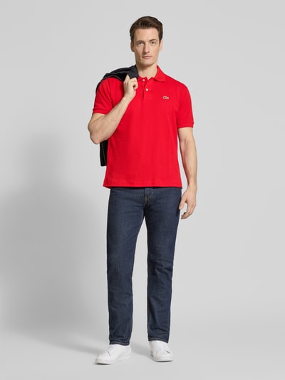 Męski model nosi Regular Fit Poloshirt aus reiner Baumwolle von Lacoste, efekt: jednolity kolor, wyhaftowane logo, kołnierzyk polo, krótki rękaw, prążkowane zakończenie rękawów, wykończenie z rozcięciami bocznymi, pika, bawełna, całopostaciowy widok z przodu.