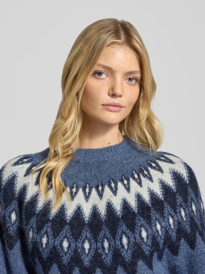 Vrouwenmodel draagt Relaxed Fit Pullover met Woll-Anteil Modell 'Jacquard' van Gina Tricot in blauw met wit-grijs zigzagpatroon, gebreide textuur, ronde hals, elastisch materiaal, bovenlichaam close-up.