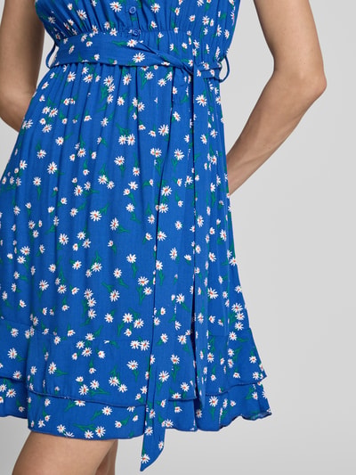 Frauenmodel trägt Minikleid aus Viskose mit Bindegürtel von Apricot, Blau mit Gänseblümchenmuster, Schmetterlingsärmel, Nahaufnahme Oberkörper. Taillierter Schnitt, V-Ausschnitt mit Rüschen, kurze Knopfleiste, Bindegürtel, Stufenrock, Rückenlänge bei Größe S: 70 cm, Brustweite bei Größe S: 44 cm.