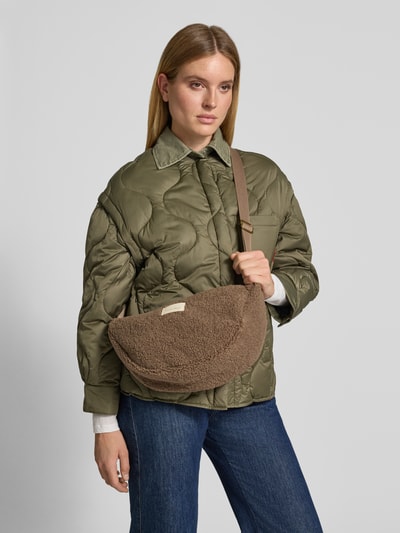 Vrouwenmodel draagt Shoulder Bag aus Teddyfell van Studio Noos in bruin, met logopatch, verstelbare schouderband, hoofvak met ritssluiting, textuur van teddybont, breedte 40 cm, lengte 20 cm, diepte 11 cm, lengte schouderband 62 cm, geheelopname van voren.