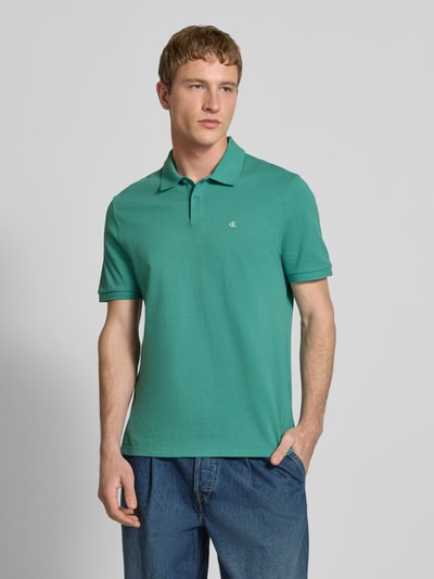 Männermodel trägt Straight Fit Poloshirt mit Label-Stitching von Calvin Klein Jeans in Grün, reine Baumwolle, Ganzkörperansicht von vorne.