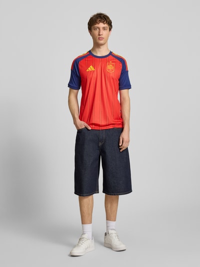Männermodel trägt Spanien Heimtrikot 2026 von adidas Sportswear, rot-blau, Optik:Allover-Muster, Slim-Fit, gestreift, Ganzkörperansicht von vorne.