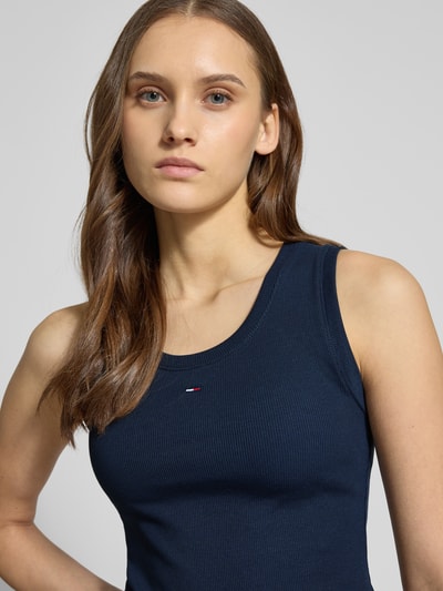 Frauenmodel trägt Slim Fit Tank Top aus Baumwoll-Mix von Tommy Jeans, unifarben dunkelblau, Logo-Detail, Feinripp, Nahaufnahme Oberkörper.