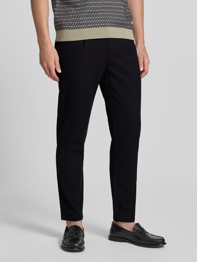 Männermodel trägt Slim Fit Stoffhose mit Viskose-Anteil von Lindbergh in Schwarz mit Strukturmuster, Nahaufnahme Unterkörper, seitlich. Elastischer Material-Mix, Bundfalten, Gesäß- und Eingrifftaschen, Tunnelzug, Knopf- und Reißverschluss, Bundweite 41 cm, Innenbeinlänge 76 cm, Struktur betont.