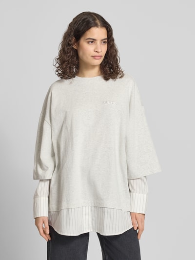 Frauenmodel trägt Oversized Longsleeve in Layering-Optik von Karo Kauer aus reiner Baumwolle, hellgrau mit Streifendetails, Label-Stitching, Rundhalsausschnitt, Rückenlänge bei Größe S 75 cm, Ganzkörperansicht von vorne.