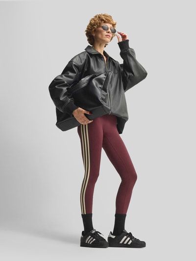 Frauenmodel trägt Slim Fit Sport-Leggings mit CLIMACOOL Technologie von adidas, bordeaux mit beigen Streifen, adidas Training, Ganzkörperansicht von vorne.