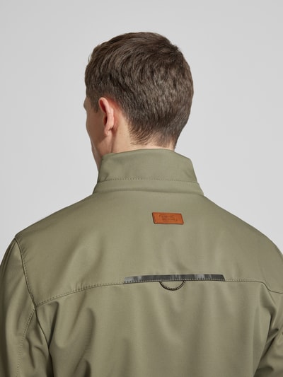 Męski model nosi Jacke mit Reißverschlusstaschen od camel active w oliwkowym kolorze, wyraźna faktura materiału, naszywka z logo, prosty krój, elastyczne zakończenia rękawów, całkowita długość tyłu w rozmiarze 50: 71 cm, szerokość ramion: 48 cm, szerokość w klatce piersiowej: 60 cm, długość rękawa: 67 cm, zdjęcie z tyłu, widok na górną część pleców.