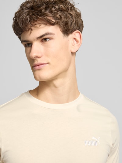Männermodel trägt T-Shirt aus reiner Baumwolle von PUMA PERFORMANCE in Beige, Rundhalsausschnitt, Label-Stitching, Nahaufnahme Oberkörper.