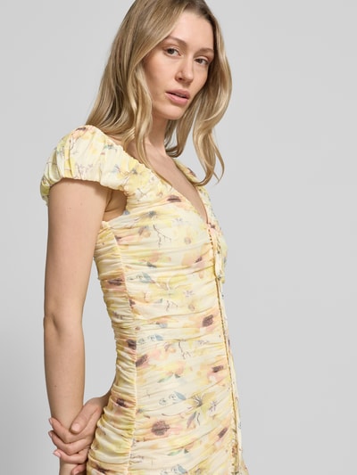 Frauenmodel trägt Midikleid mit Drapierungen und V-Ausschnitt von Little Mistress in sanftem Gelb mit Blumen, Material-Mix mit Stretch-Anteil, figurbetonter Schnitt, Rückenlänge bei Größe 36: 120 cm, Nahaufnahme Oberkörper.
