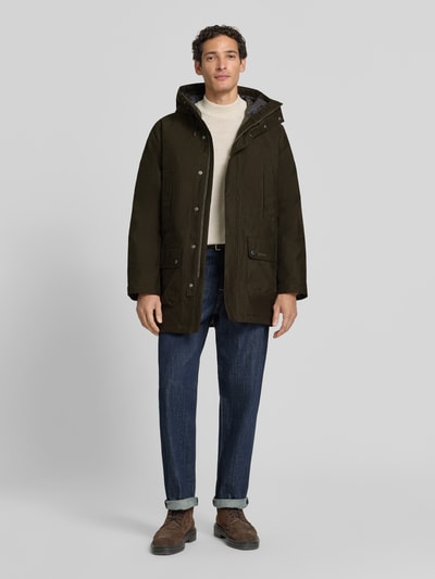 Männermodel trägt Regular Fit Funktionsjacke mit Kapuze von Barbour in Dunkelgrün, kombinierbar mit Jeans, Ganzkörperansicht von vorne.