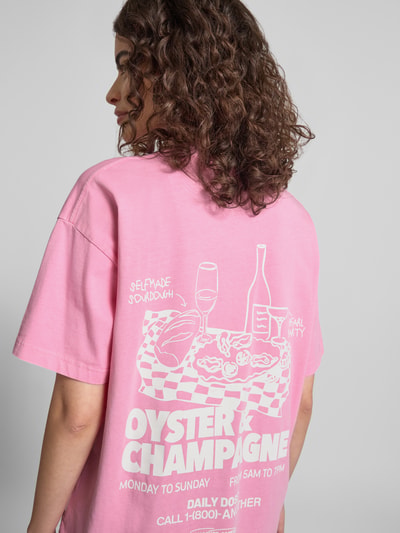 Frauenmodel trägt Oversized T-Shirt mit Logo-Print von ANOTHER COTTON LAB in Rosa, Baumwolle, lockerer Schnitt, Rückseite mit weißem Print, Ganzkörperansicht Rückansicht.