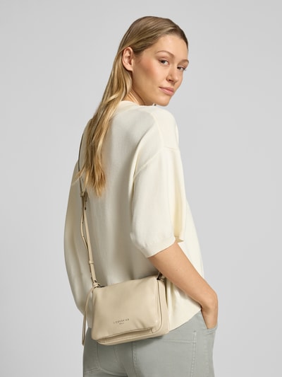 Frauenmodel trägt Crossbody Bag mit Logo-Prägung Modell 'Nina' von LIEBESKIND BERLIN in Beige, sanft strukturierte Oberfläche, Ganzkörperansicht Rückansicht. Geteiltes Hauptfach mit Reißverschluss, Verstellbarer Schulterriemen, Breite 18 cm, Länge 13 cm, Tiefe 7 cm, Länge Schulterriemen 119 cm.