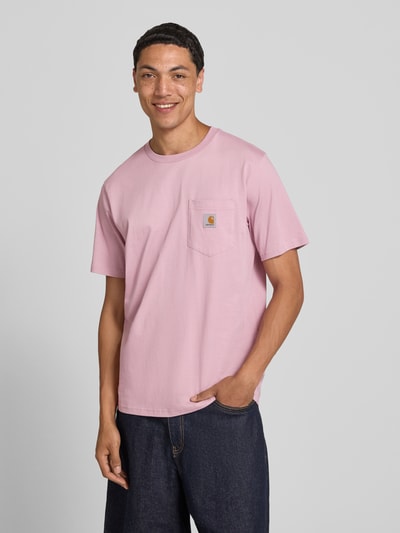 Männermodel trägt Regular Fit T-Shirt mit Brusttasche von Carhartt Work In Progress in Rosa, Reine Baumwolle, Label-Patch, Ganzkörperansicht von vorne. Herren T-Shirt mit Rundhalsausschnitt, Rückenlänge bei Größe M 71 cm.