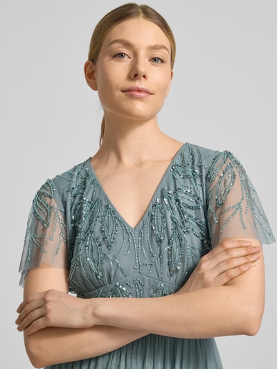 Kobiece modelka nosi sukienka wieczorowa 'Abendkleid mit Ziersteinbesatz' od Christian Berg Cocktail, linia a, dekolt w serek, marszczenia, obszycie ozdobnymi kamieniami, zamek błyskawiczny z tyłu, długa sukienka, długość tyłu w rozmiarze 36: 140 cm, szerokość w rozmiarze 36: 38 cm, długość rękawów w rozmiarze 36: 21 cm, niebiesko-zielone odcienie, geometryczne wzory, tekstura tiulu, detaliczne zdobienia, zbliżenie na górną część ciała, przód