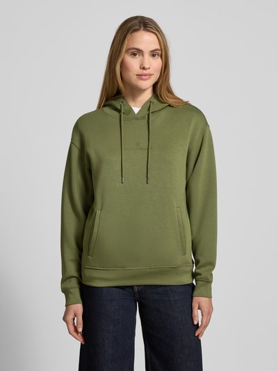 Modelka kobieca ma na sobie zielony Hoodie aus Viskose-Mix mit Logo Modell 'IMA' od MSCH Copenhagen, regular fit, kieszenie, widok z przodu całej sylwetki.