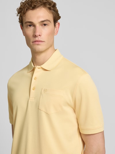 Männermodel trägt Regular Fit Poloshirt mit Brusttasche und Label-Stitching von bugatti in Hellgelb, glatte Textur, Nahaufnahme Oberkörper.