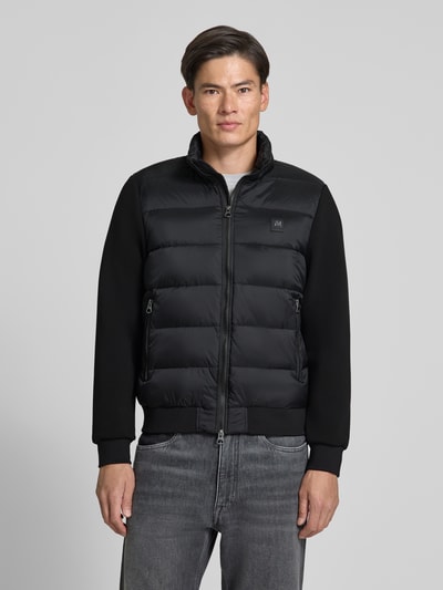 Männermodel trägt Jacke mit Label-Patch und Stehkragen von Antony Morato in Schwarz, Zweiwege-Reißverschluss, Ganzkörperansicht von vorne.