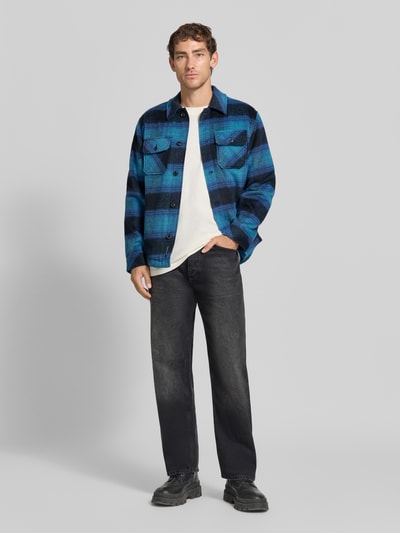 Männermodel trägt Regular Fit Hemdjacke mit Brusttaschen von Scotch & Soda im blauen Allover-Karomuster, Ganzkörperansicht von vorne. Mix mit Woll-Anteil und Kentkragen, Knopfleiste, Rückenlänge in Größe M 72 cm.