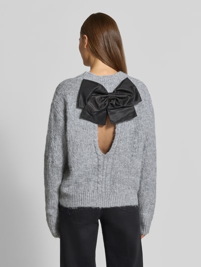 Frauenmodel trägt Regular Fit Strickpullover aus elastischem Woll-Mix von Apricot, szary, okrągły dekolt, prążkowane wykończenia, długość tyłu 55 cm, długość rękawów 68 cm, materiał miękki, z dużą czarną kokardą, widoczny otwór na plecach, Ganzkörperansicht Rückansicht.