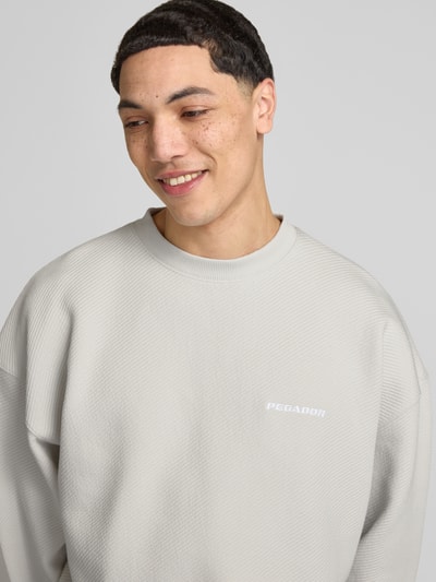 Mannenmodel draagt Oversized Fit Sweatshirt met logo-stitching model 'Tate' van Pegador, structuurpatroon, ronde hals, elastische boorden, katoenmix, oversized fit, nahaufnahme bovenlichaam.