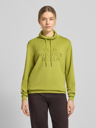 Modelka kobieca nosi Sweatshirt mit Stehkragen und Statement-Print od Soyaconcept, mieszanka materiałów z domieszką modalu, krój regular fit, nadruk z napisem, stójka, tunel, widok całej sylwetki z przodu.