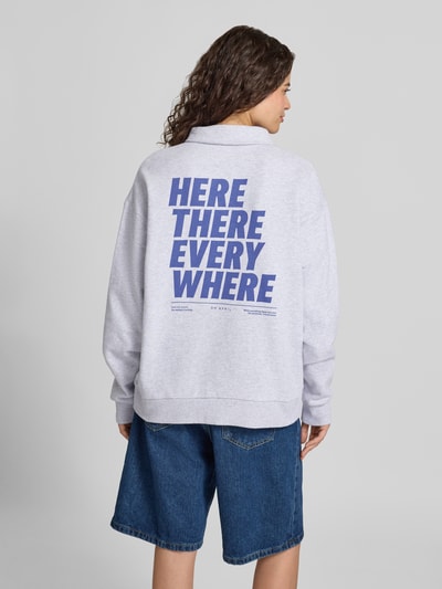 Frauenmodel trägt Oversized Sweatshirt mit Polokragen und Label-Print von OH APRIL, graue Baumwolle, blauer Print, Ganzkörperansicht Rückansicht.