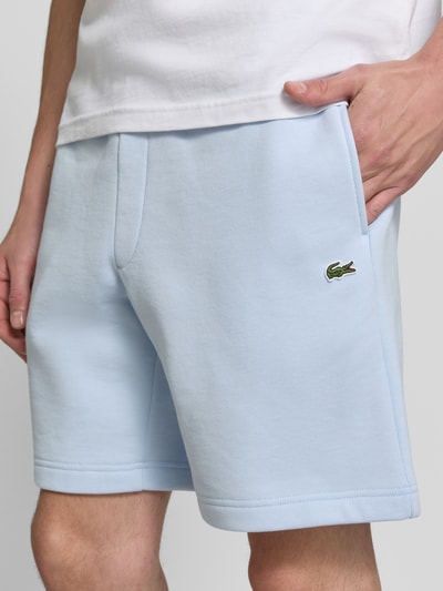 Männermodel trägt hellblaue Relaxed Fit Sweatshorts aus Baumwoll-Mix von Lacoste, glatte Oberfläche, Nahaufnahme Oberkörper, Herren Sweatshorts von Lacoste.