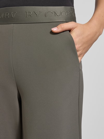 Vrouwenmodel draagt Stoffen broek in verkorte pasvorm Model 'ELENA' van Cambio, materiaalmix, los model, steekzakken, elastische band met logo, detailopname.