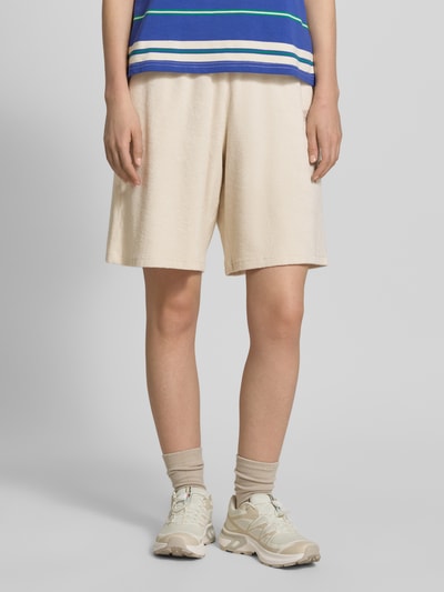 Vrouwenmodel draagt Sweatshorts mit Eingrifftaschen und Logo-Stitching Modell 'FUXOW' van American Vintage in beige, pure katoen, losse fit, elastische tailleband, Franse steekzakken, detailopname benen, vooraanzicht.