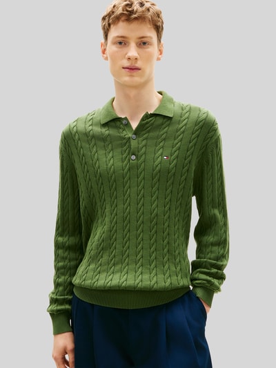 Männermodel trägt Regular Fit Strickpullover aus reiner Baumwolle von Tommy Hilfiger in Grün mit Zopfmuster, Polokragen, Logo, Ganzkörperansicht von vorne.