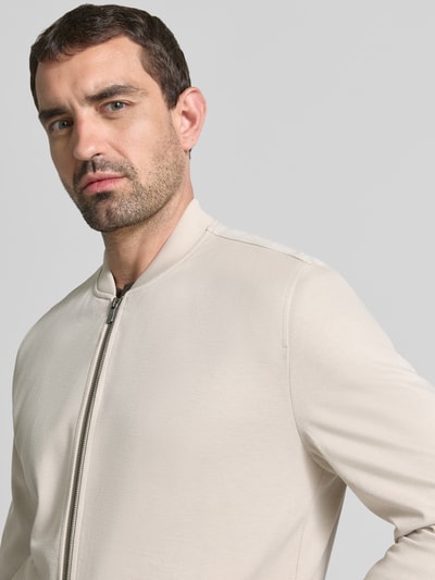 Männermodel trägt Jacke aus Viskose-Mix von MCNEAL in Beige mit Stehkragen und Reißverschluss, Nahaufnahme Oberkörper, gerader Schnitt. Rückenlänge 66 cm, Schulterbreite 45 cm, Brustweite 52 cm, Ärmellänge 68 cm, Stretch-Anteil, Eingrifftaschen.