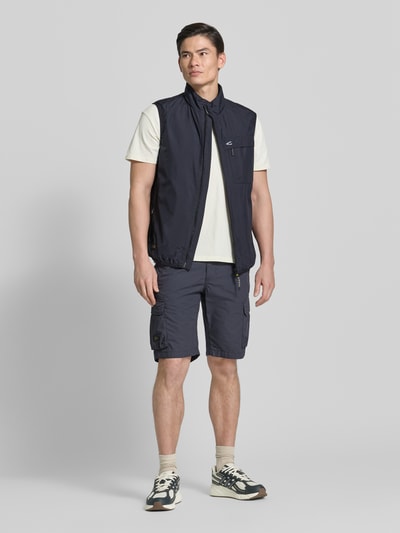 Männermodel trägt Regular Fit Weste mit gefüttertem Stehkragen von camel active in Dunkelblau mit Brusttasche, Reißverschluss, Eingrifftaschen, elastischer Bund, Rückenlänge 64 cm, Schulterbreite 45 cm, Brustweite 60 cm, Ganzkörperansicht von vorne.