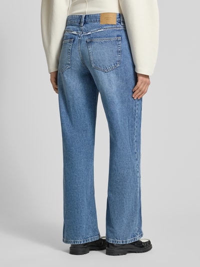 Männermodel trägt Wide Leg Jeans mit Fransennähten von Gina Tricot aus bawełna, krój wide fit, wpuszczane kieszenie, kieszenie z tyłu, zapięcie na guzik i zamek błyskawiczny, szerokość w rozmiarze 38: 39 cm, długość wewnętrzna nogawki w rozmiarze 38: 77 cm, kolor niebieski, faktura denimowa, ganzkörperansicht rückansicht.
