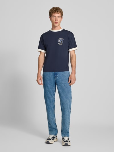 Mężczyzna nosi Slim Straight Fit Jeans aus Baumwoll-Mix Modell 'RYAN' von Tommy Jeans, jasnoniebieski denim, tekstura gładka, Herren Bomberjacke / Blouson von Tommy Jeans, Ganzkörperansicht von vorne